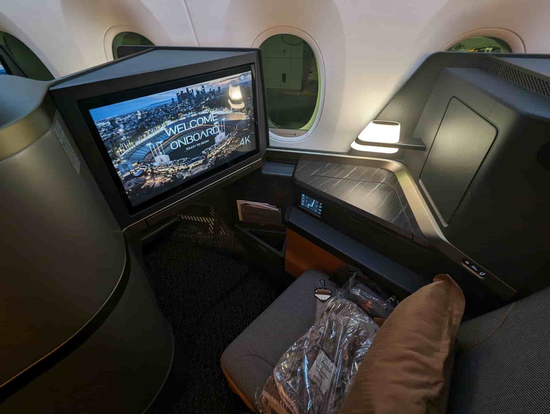 Modern business class airplane seat with large personal screen, side table, and window view, set in a private pod-style cabin