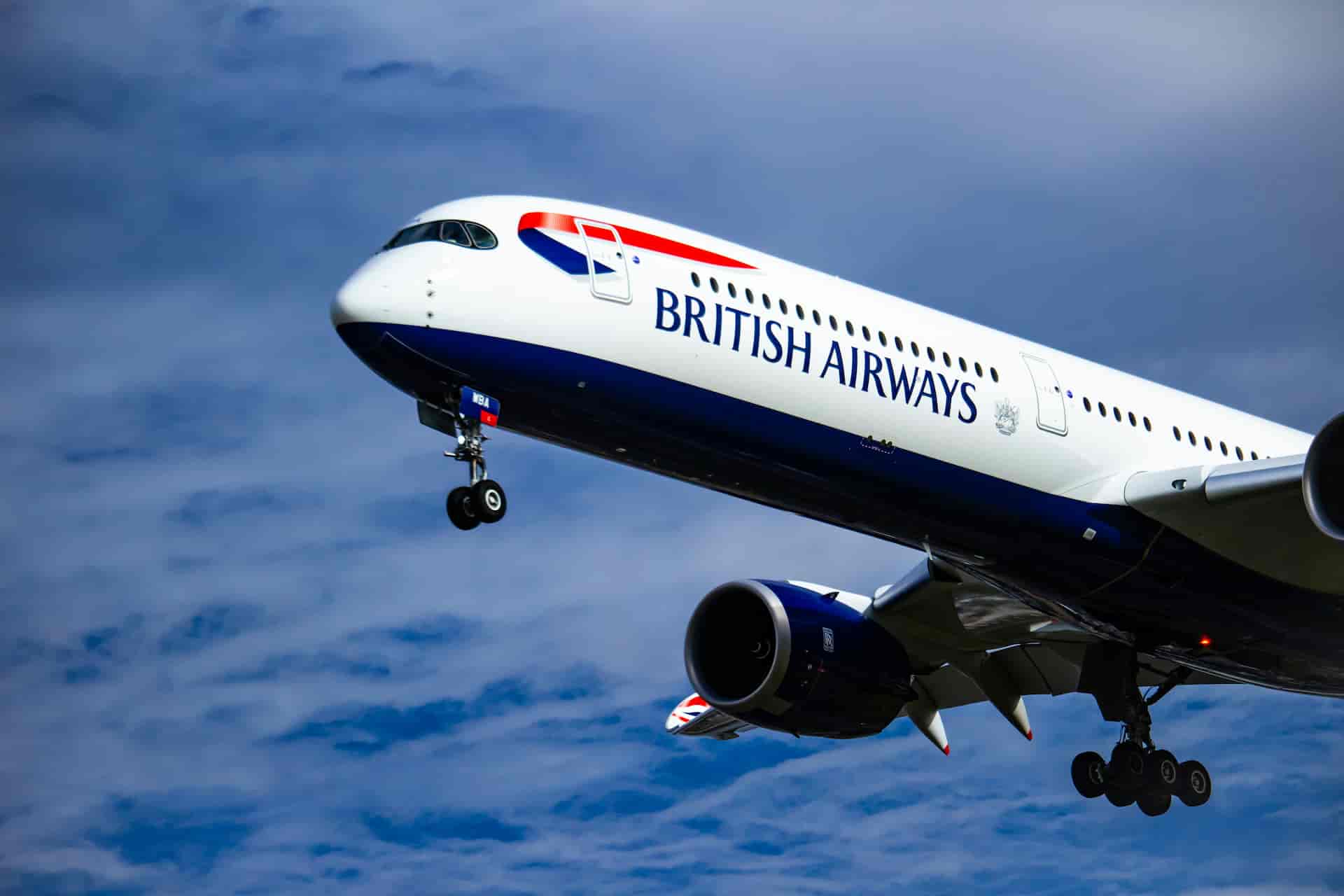 A British Airways passenger airplane taking off into a blue sky with light clouds, landing gear still extended.