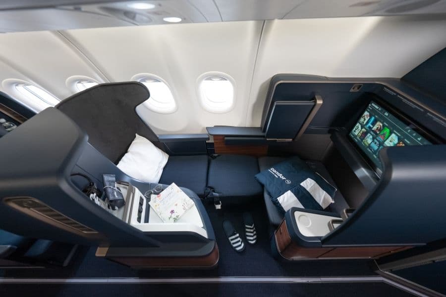 A spacious business class airplane seat with a lie-flat bed, personal screen, storage compartments, and window views.